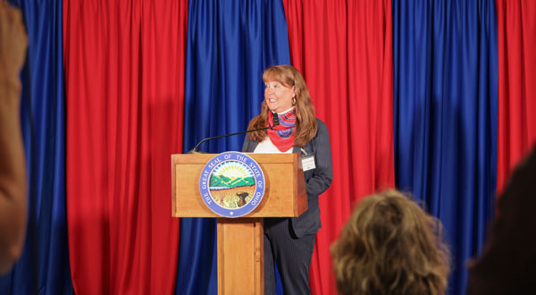 Woman at a podium that has Ohio's state seal. There is blue and red draping in the background.