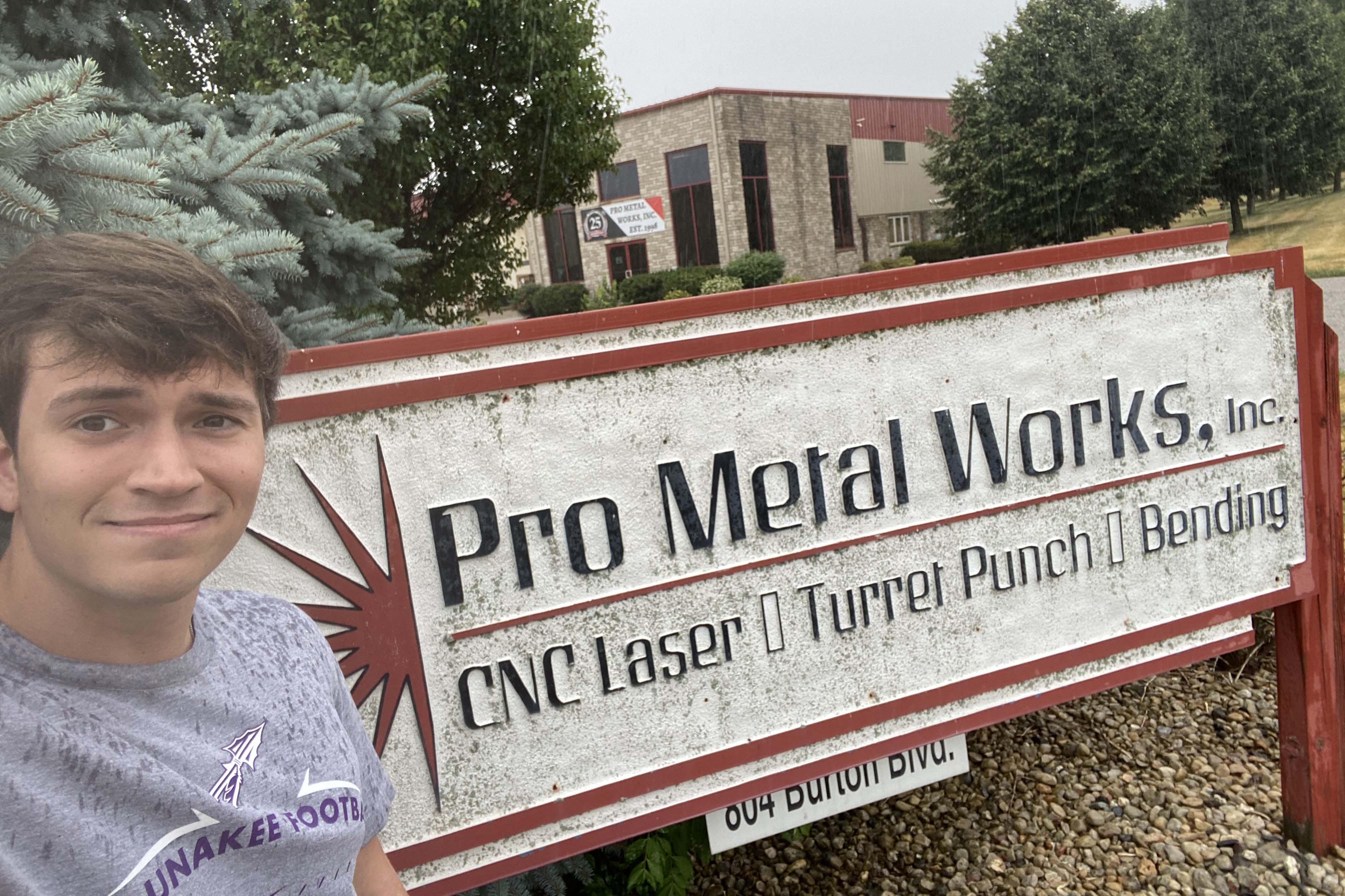 Connor Carroll taking a selfie outside in front of the Pro Metal sign.