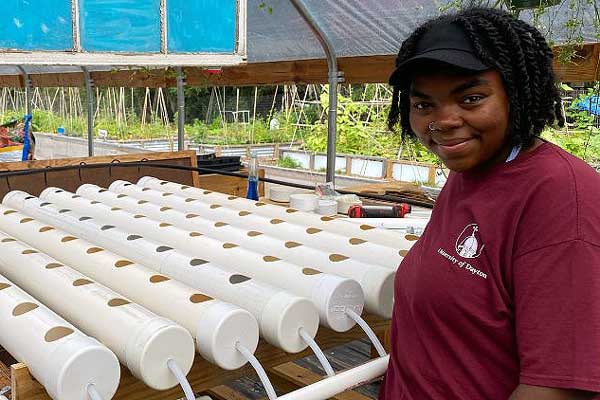 A student smiling at the camera in front of hydroponics systems.