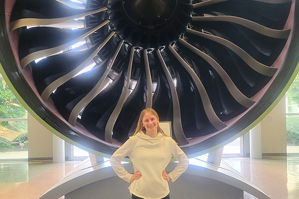Female student posing for camera in front of airplane engine.
