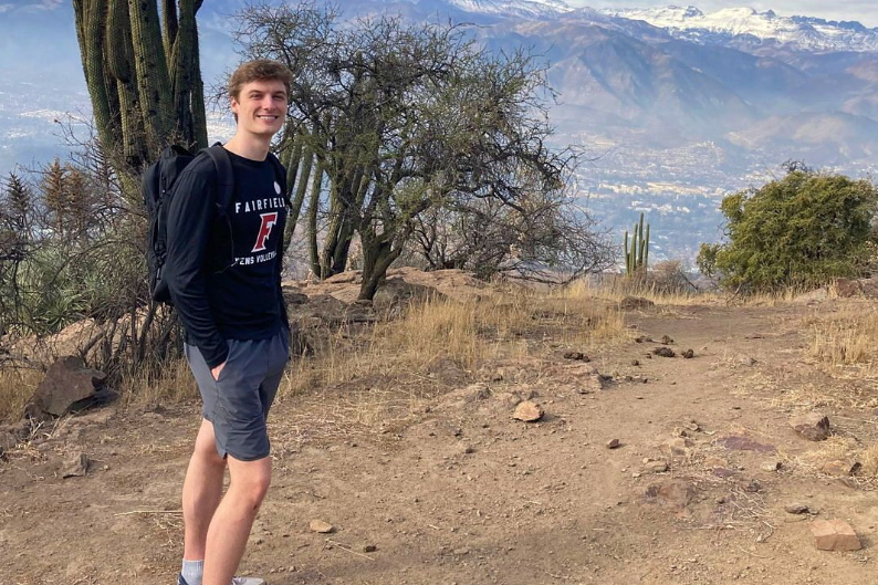Student David Albrecht outside standing on top of a mountain area. There is a cactus behind him to the left.