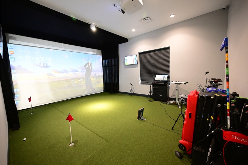 NCR Player Development Center with a large monitor and putting green. There is also a University of Dayton golf bag.
