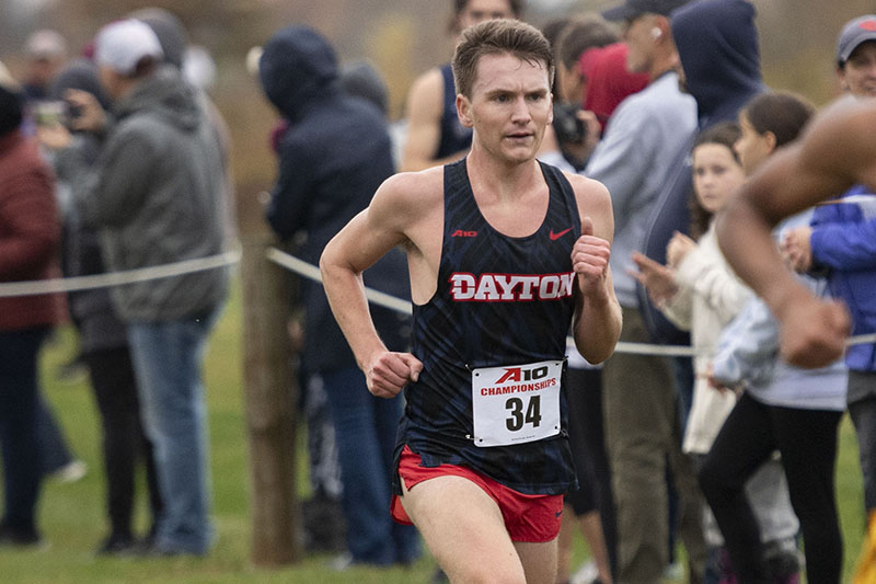 Close-up of Sam Duncan running in a cross country meet with spectators in the background