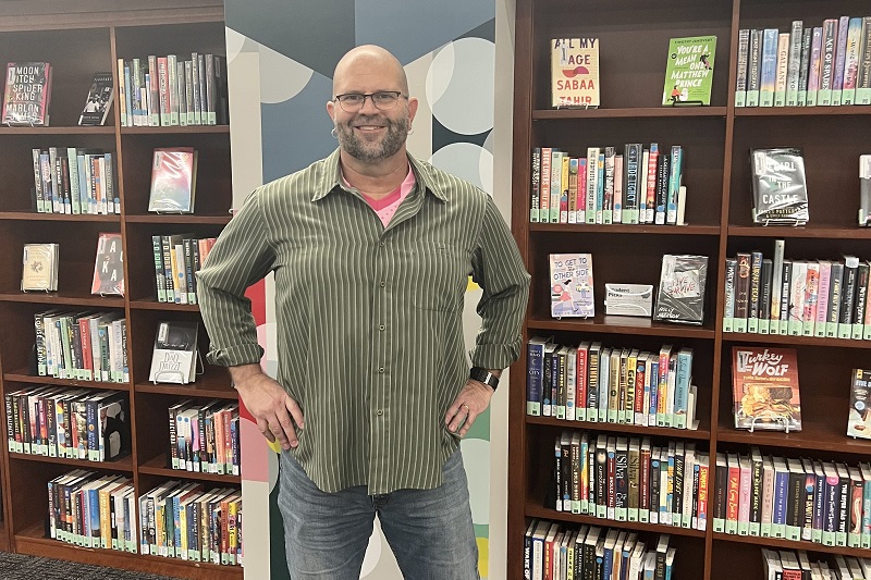 The blog author standing in front of shelves of leisure reading books in Roesch Library's lobby