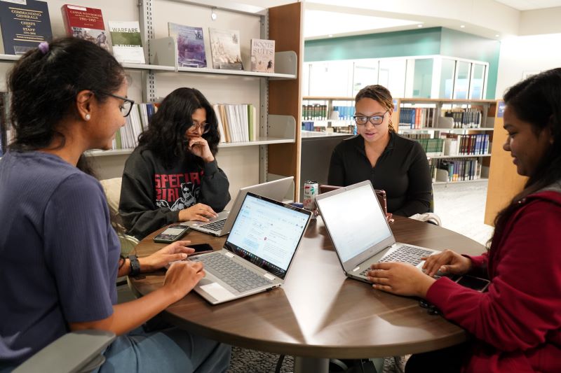 four students at a library table with their laptops open