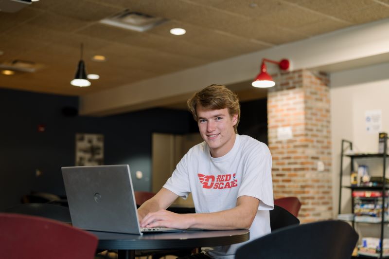 a student wearing a Flyers t-shirt on a laptop in a dining hall