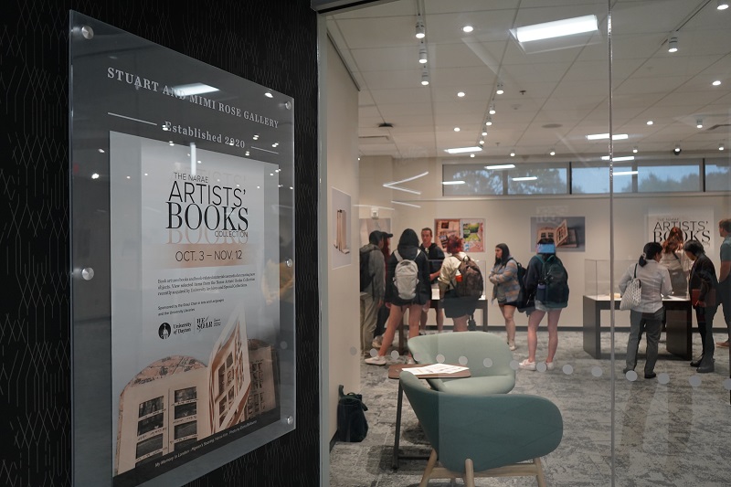 Photo shows the Stuart and Mimi Rose Gallery at the University of Dayton. Students are milling about, looking at the artist books in the display cases.