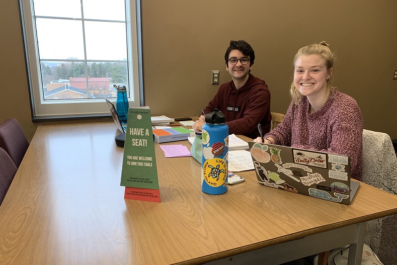 Students at a table with a green "have a seat" table tent