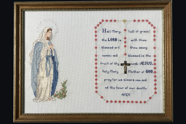 Needlepoint depicting the Blessed Virgin Mary on the left and the words to the Hail Mary on the right inside a rosary