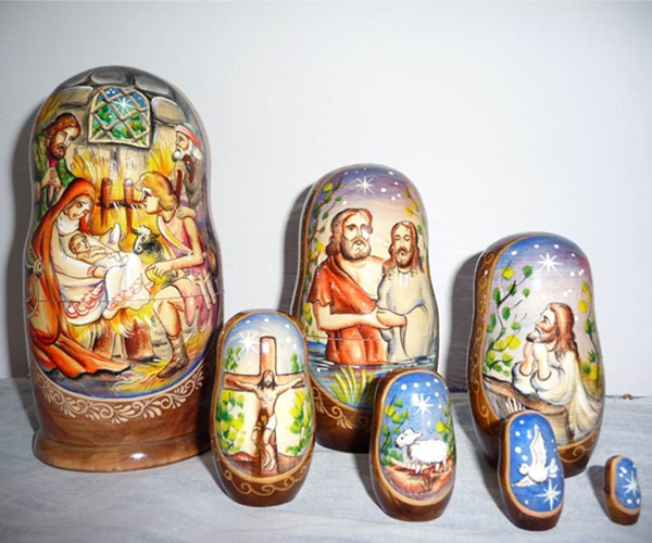 A set of seven nesting dolls. From largest to smallest: depiction of Nativity, John baptizing Jesus in the Jordan, Jesus praying in the garden, Jesus on the Cross, a white dove, a star
