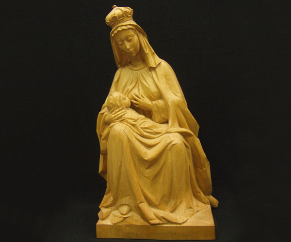 Carved wooden statue of the crowned Madonna sitting with Infant Jesus resting on her lap while nursing.  