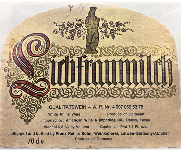 Label removed from a bottle of “Liebfraumilch white Rhine wine produced in Germany. Shipped and bottled by Franz Reh & Sohn, Weinkellerei, Leiwen-Germany-Abfüller.” The label is a light golden paper, rounded at the top. A gold, outlined in black, standing Madonna nursing the Infant Jesus in the middle of illustrated grapevines is at the top above “Liebfraumilch” which is set in an old style script. The “L” is red and the rest of the letters are gold. “Liebraumilch” is surrounded by gold scrolls.