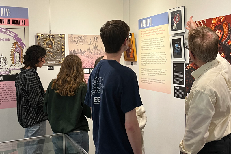 A professor teaches four students in a gallery exhibit of Ukrainian artwork of Mary. 