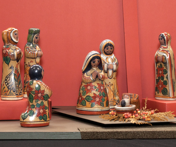 Clay figures of Jesus, Mary, Joseph, an angel, a shepherd, and three wise men are painted with red poinsettias and other natural elements.
