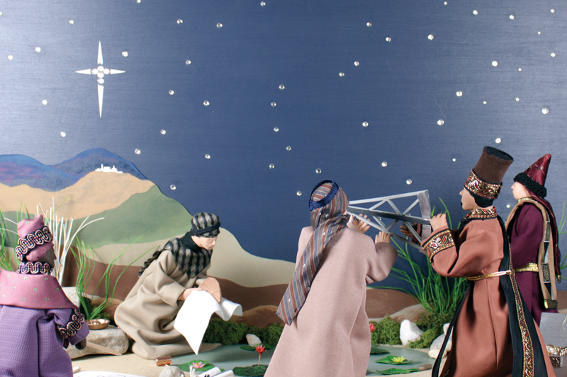 Dolls depicting Magi and an additional traveler use maps and a tool called an astrolabe to plan their route. Hills and a starry sky with a large star in the background.