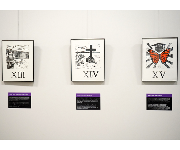 Prints on white paper hang in thin black frames on a white wall. The prints use black and orange ink to depict Stations of the Cross with a monarch butterfly rather than Jesus Christ. Underneath each print is a black label with a purple strip across the top with white text. 