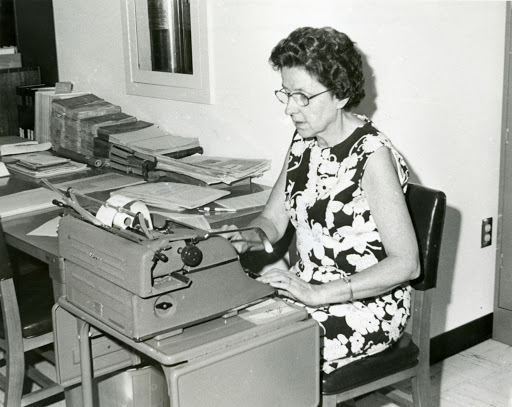 Black and white photograph of Mildred Sutton sitting and working at a typewriter circa 1980s.