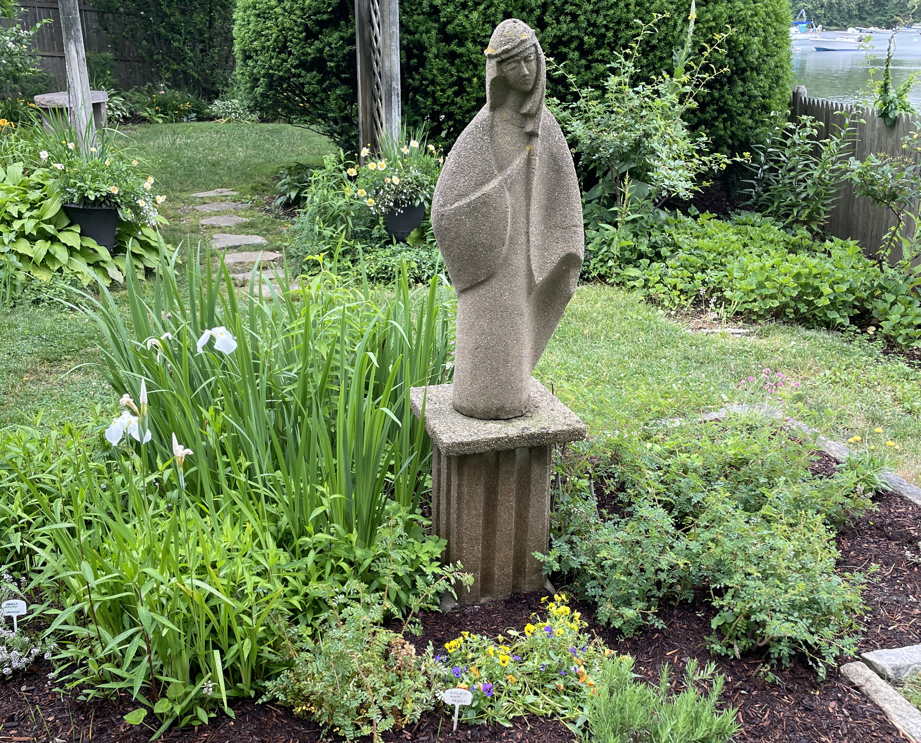 Current day photo of the Virgin Mary statue surrounded by flowers and plants