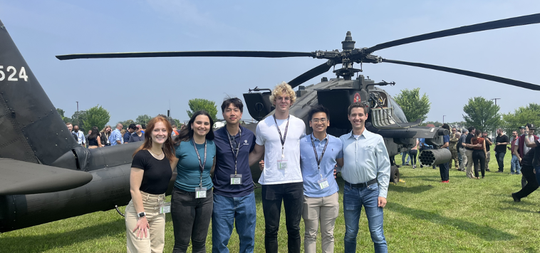 A group of students smiling at the camera in front of a helicopter