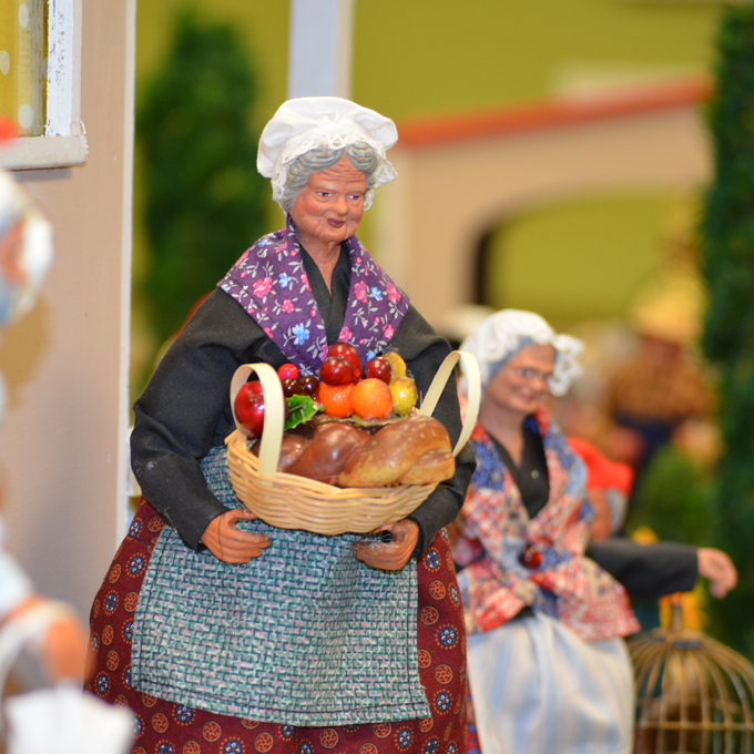 figure of an elderly female holding a basket of fruit and bread