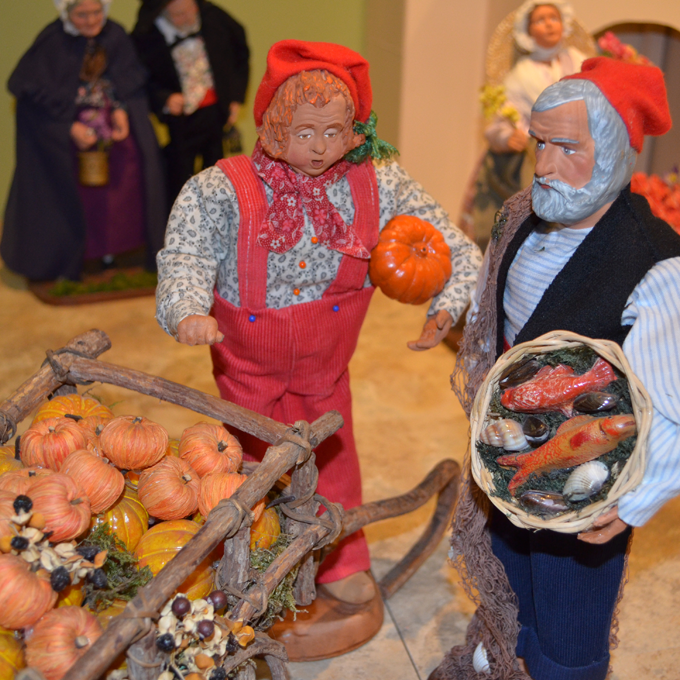 male figure with a cart of pumpkins and a male figure with a basket of fish