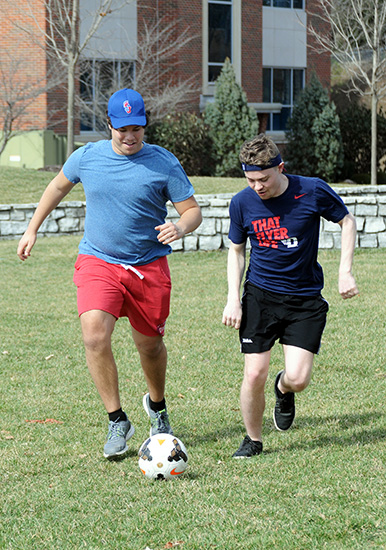 Two students play soccer in the warm weather. 