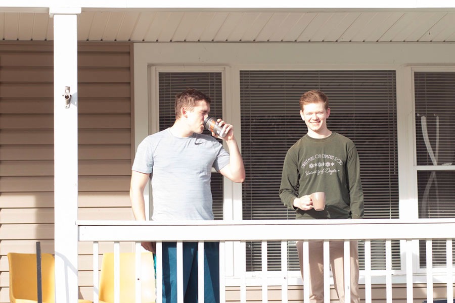 Two students stand on a porch and drink coffee