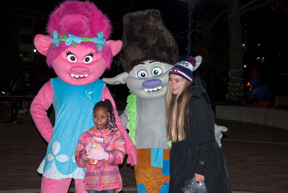A student and child pose with costumed characters from Trolls.