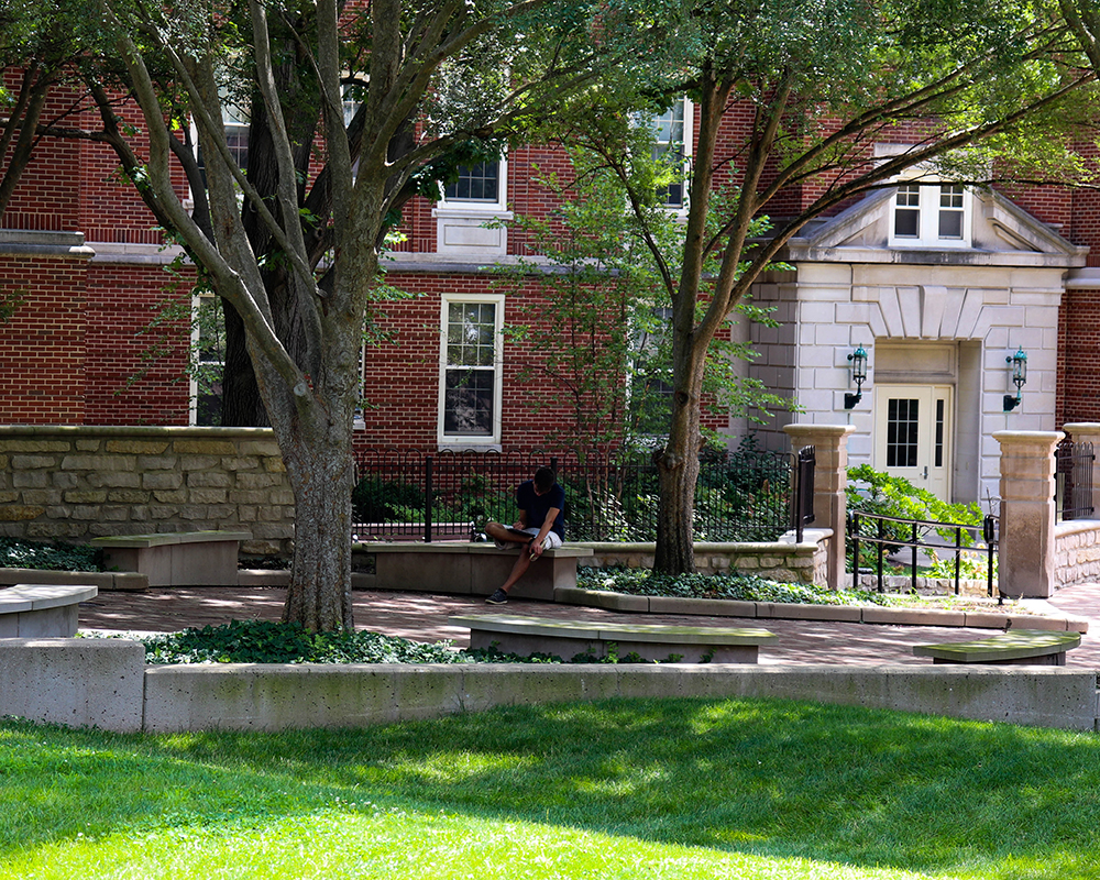 A student sits outside Alumni Hall and reads