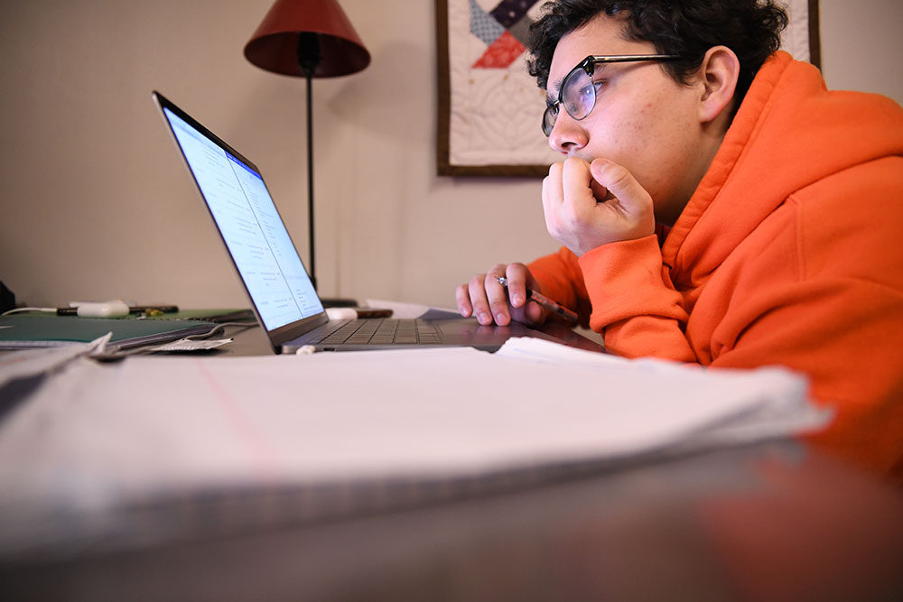 Man in orange sweatshirt works on his computer