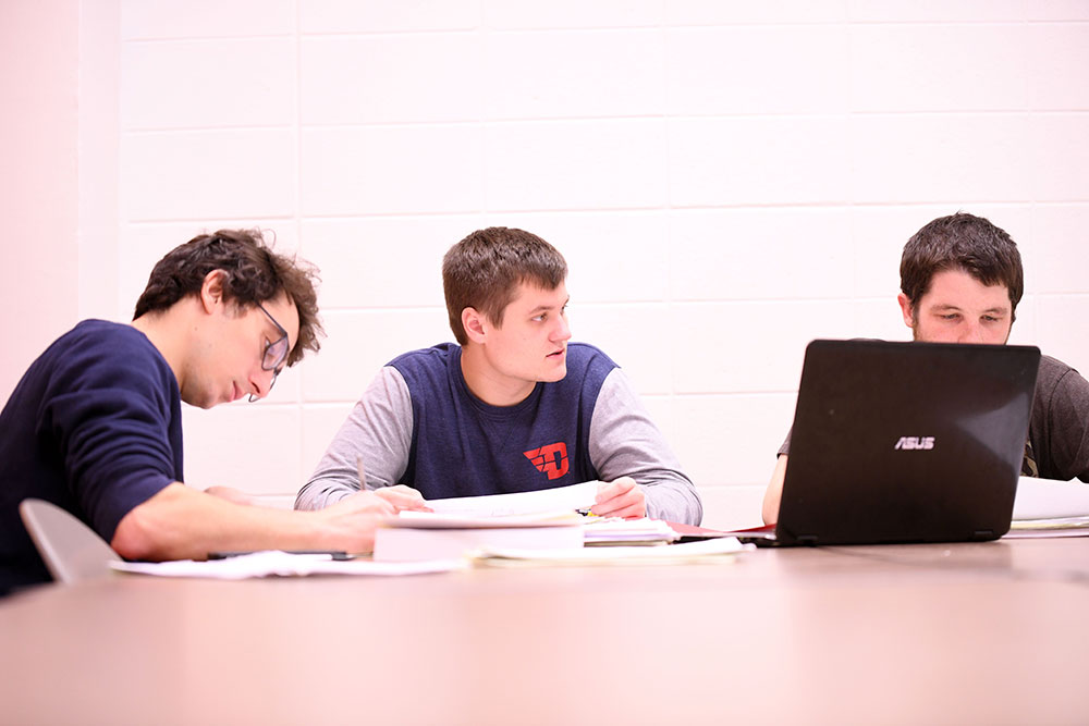 Three men sit at a table to study. 