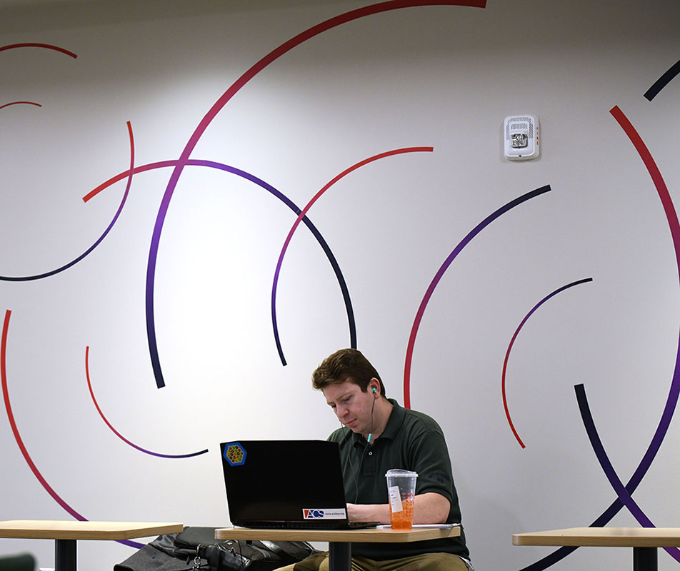 Man at a computer in front of a wall with red and blue swirls
