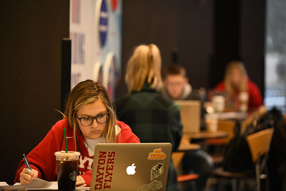 A student in a Dayton Flyers jersey studies at a computer with a Dayton Flyers sticker