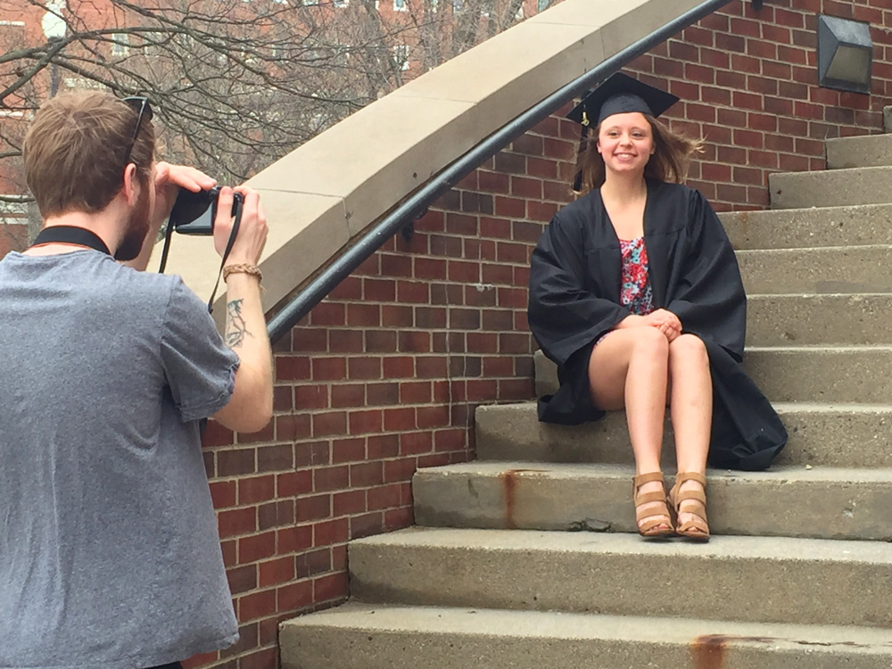 Man takes a photo of a woman in a cap and gown
