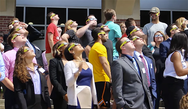 students with protective glasses look up at the eclipse