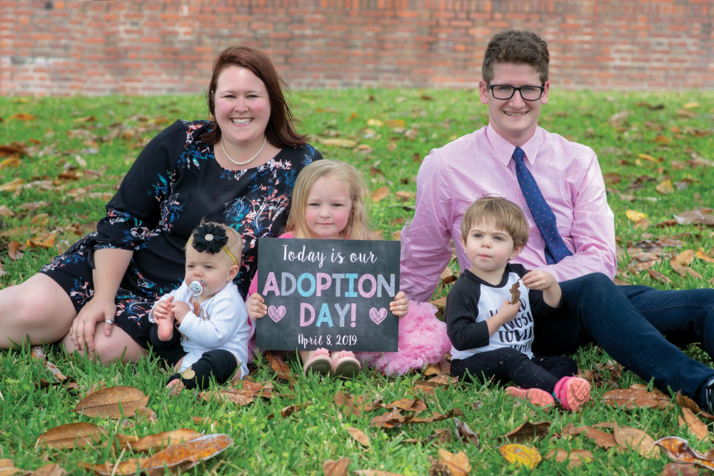 Mom, Dad and three children pose with a sign saying it's adoption day. 