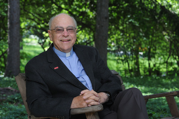 Father Norbert Burns, smiling, sitting on a bench with trees in the background