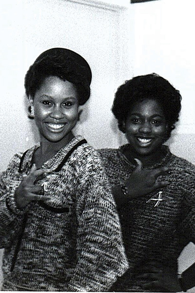 Two woman display the hand symbol for their sorority. 