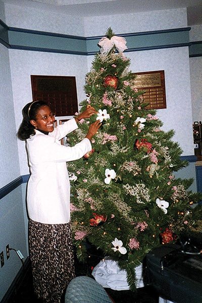 A woman puts ornaments on a holiday tree. 