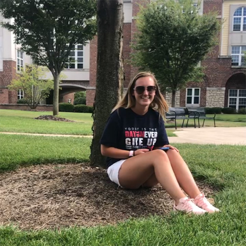 student sits under a tree on a college campus