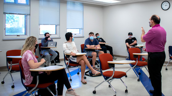 Professor teaches class with students, all wearing face coverings