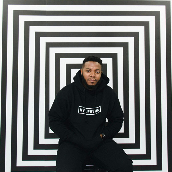 LaFlore in a black sweatshirt standing in front of a black-and-white spiral backdrop