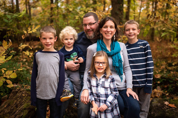 AJ Grimm with her husband and four children all dressed in blue standing in the woods in autumn