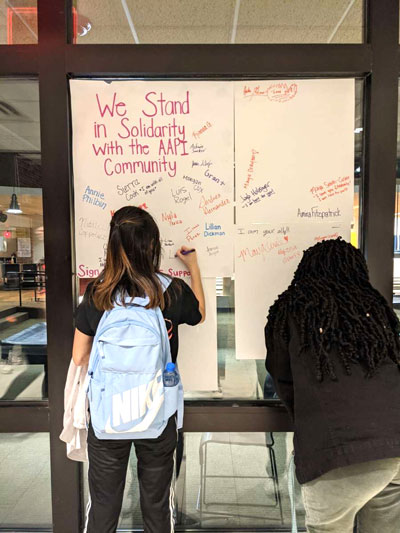 Students add their names in colorful markers to a poster of support for the Asian American and Pacific Islander community. 