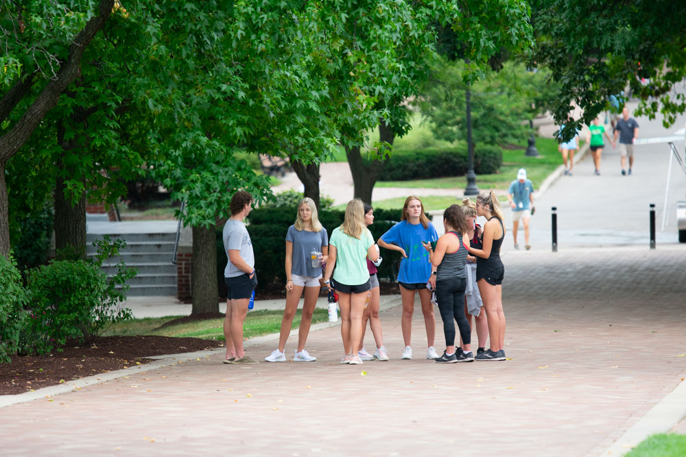 Students stand and talk on the brick sidewalk
