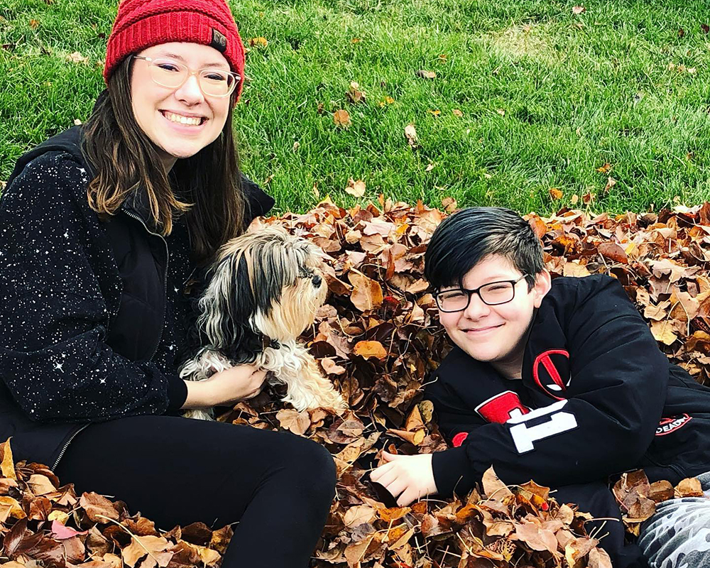 kids and dog sit in a pile of fall leaves