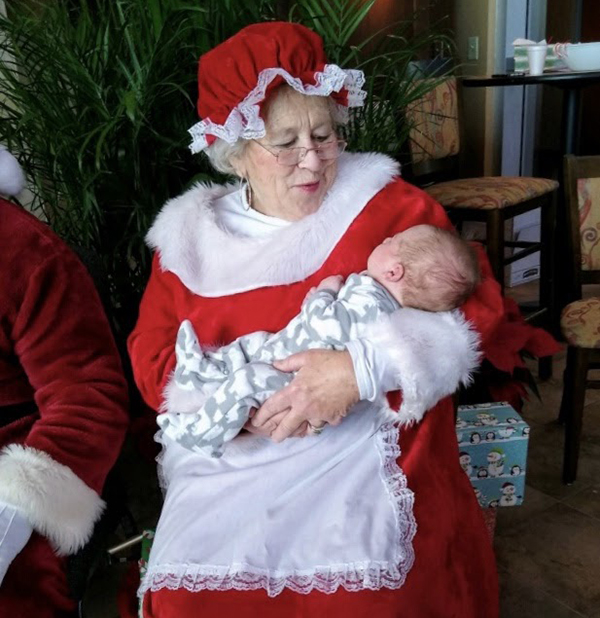 Judy O'Rourke dressed as Mrs. Claus holding a baby.