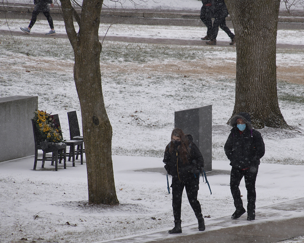 Two students walk to class as snow falls