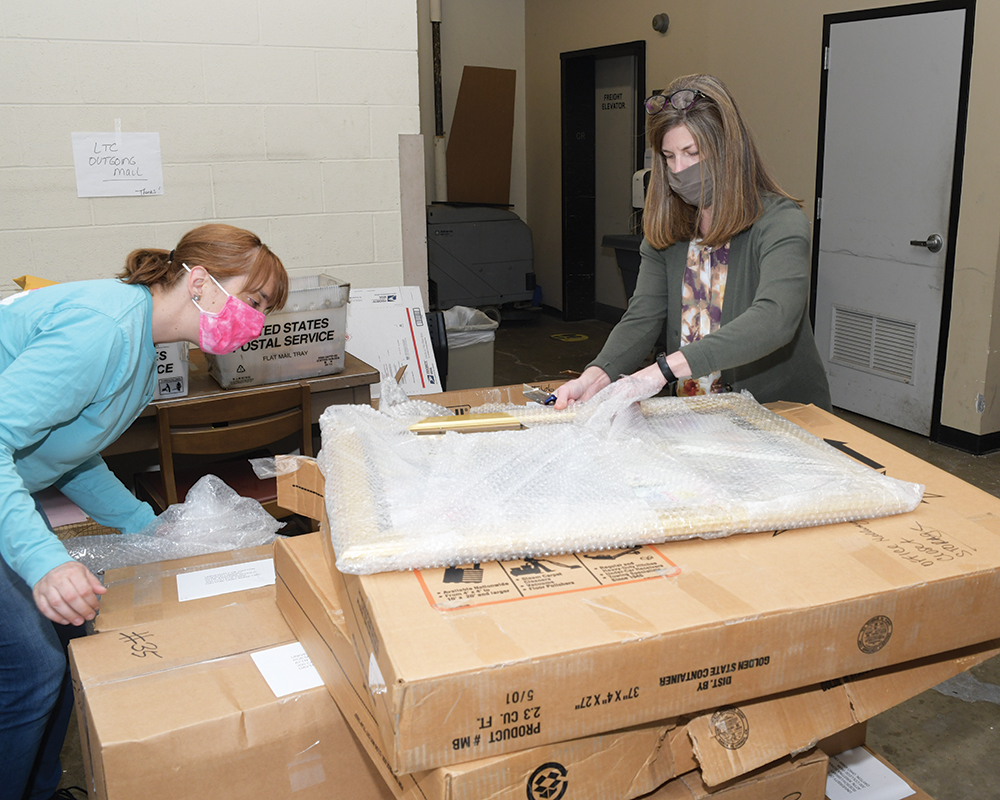 Two women unpack a shipment of cardboard boxes