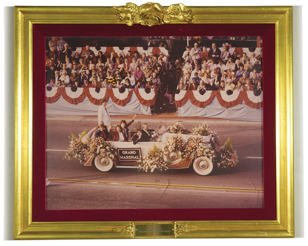 A framed photo of people riding in a car in a parade